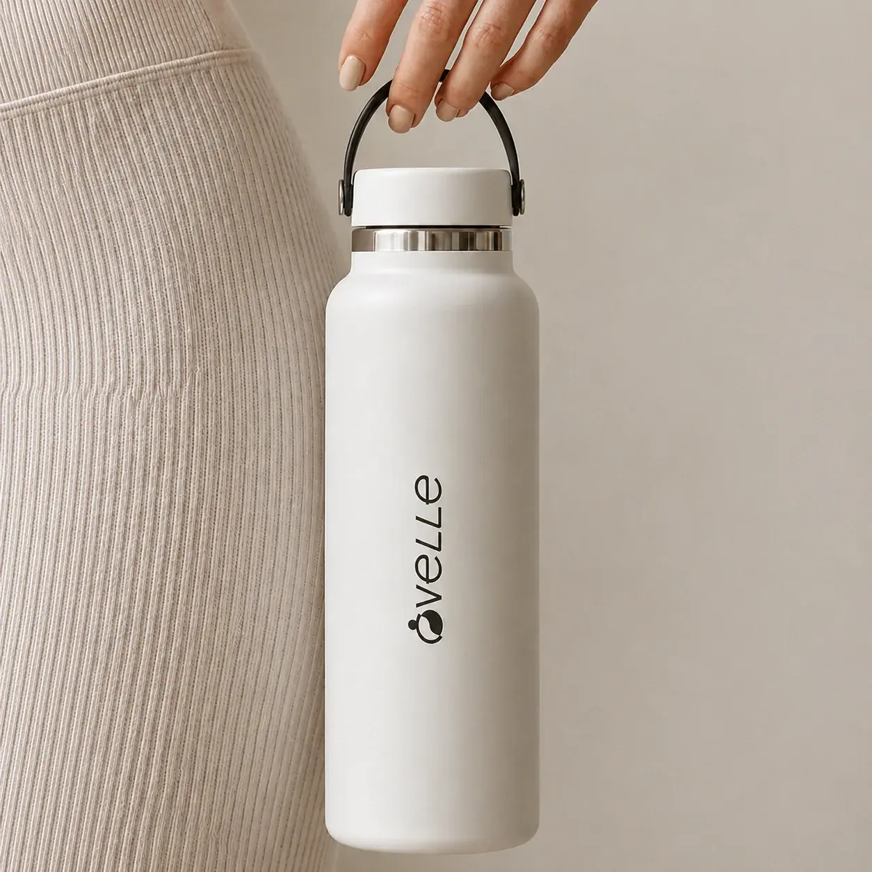 White Ovelle water bottle held beside neutral ribbed activewear.