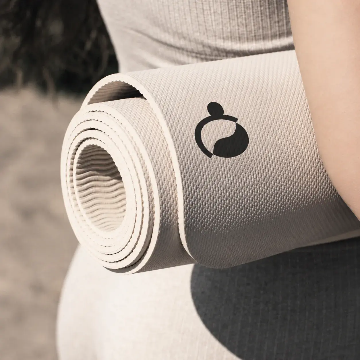Rolled neutral exercise mat with the Ovelle symbol carried beside activewear.