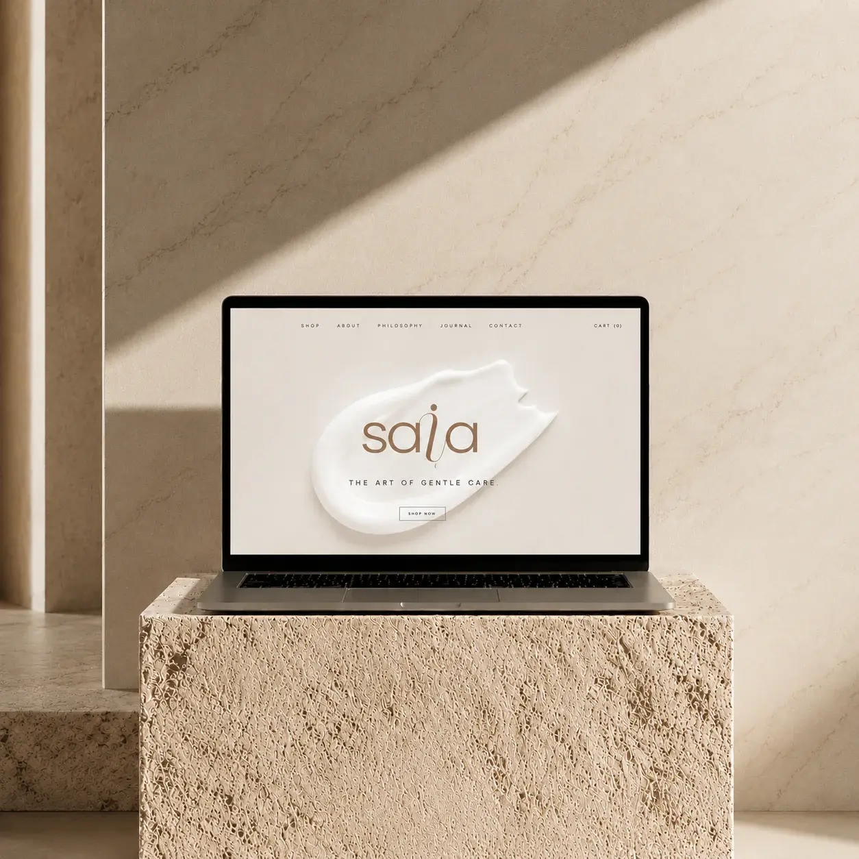 Laptop displaying the SAIA Skincare website on a warm textured stone plinth.