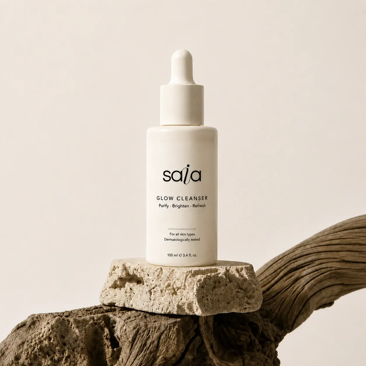 SAIA Glow Cleanser dropper bottle displayed on warm sculptural stone forms.