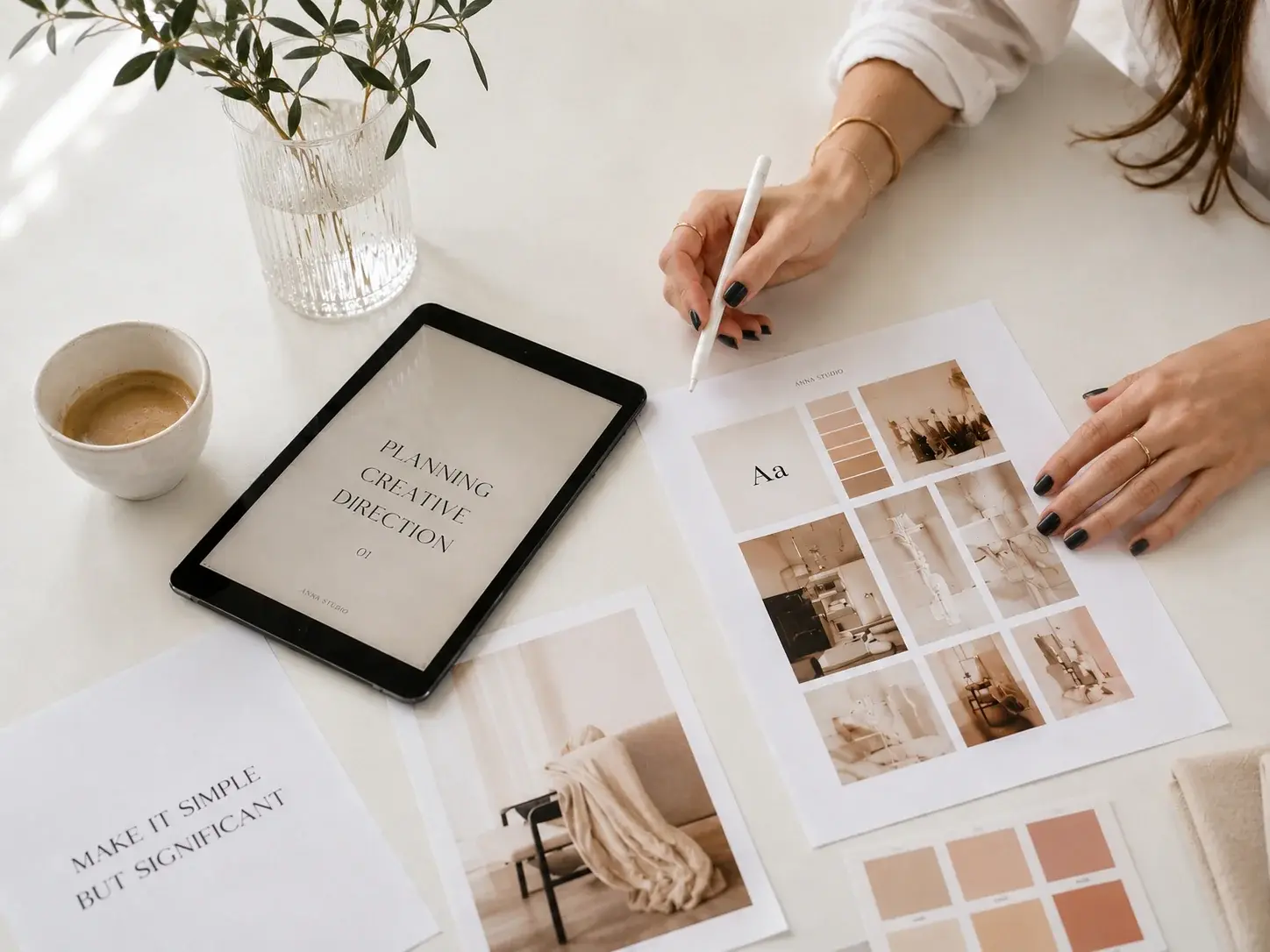 Designer planning a creative direction with a tablet, printed moodboard and color references at a bright studio desk.