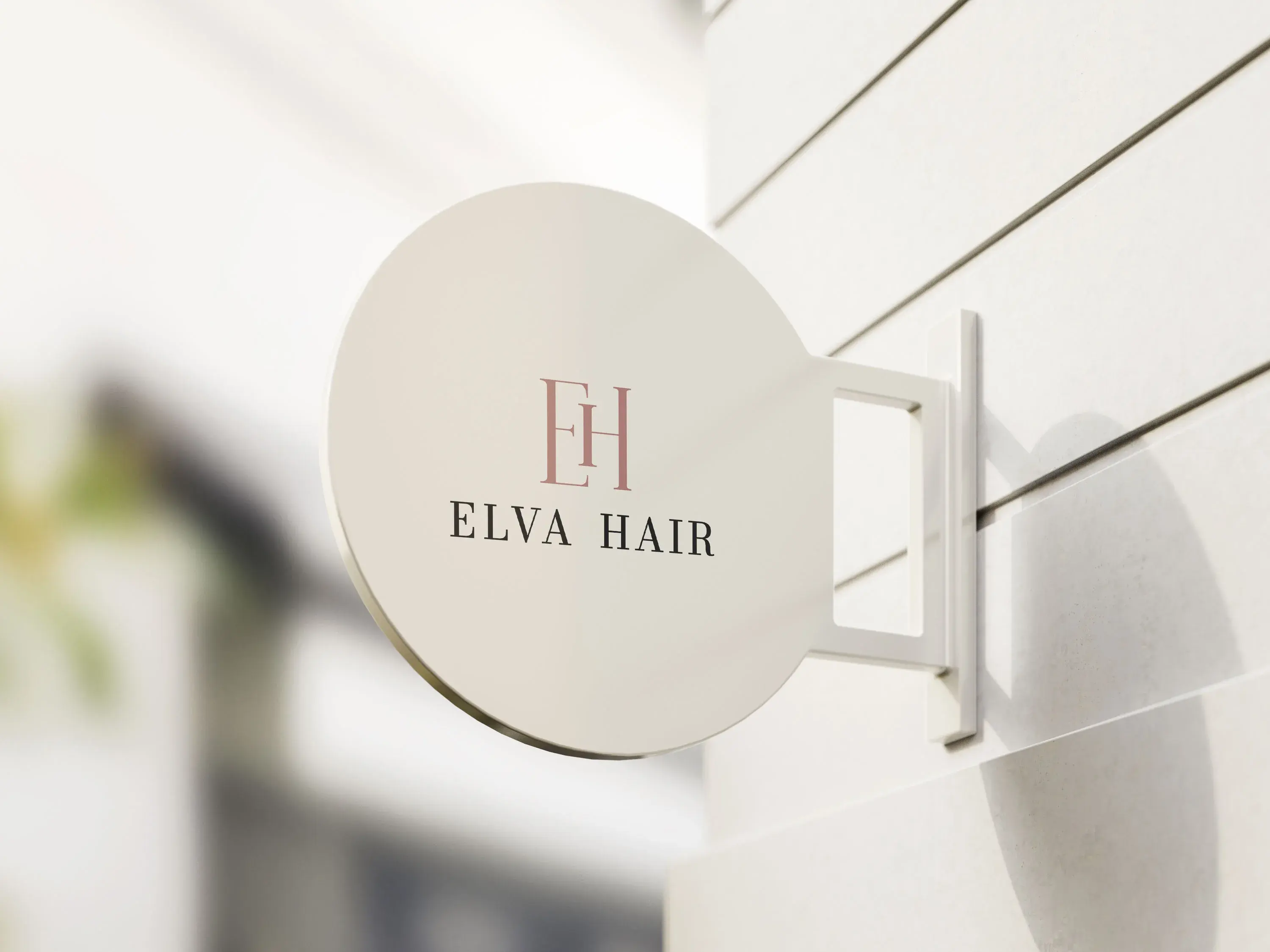 ELVA Hair exterior round sign mockup with blush monogram and serif wordmark on a light facade.