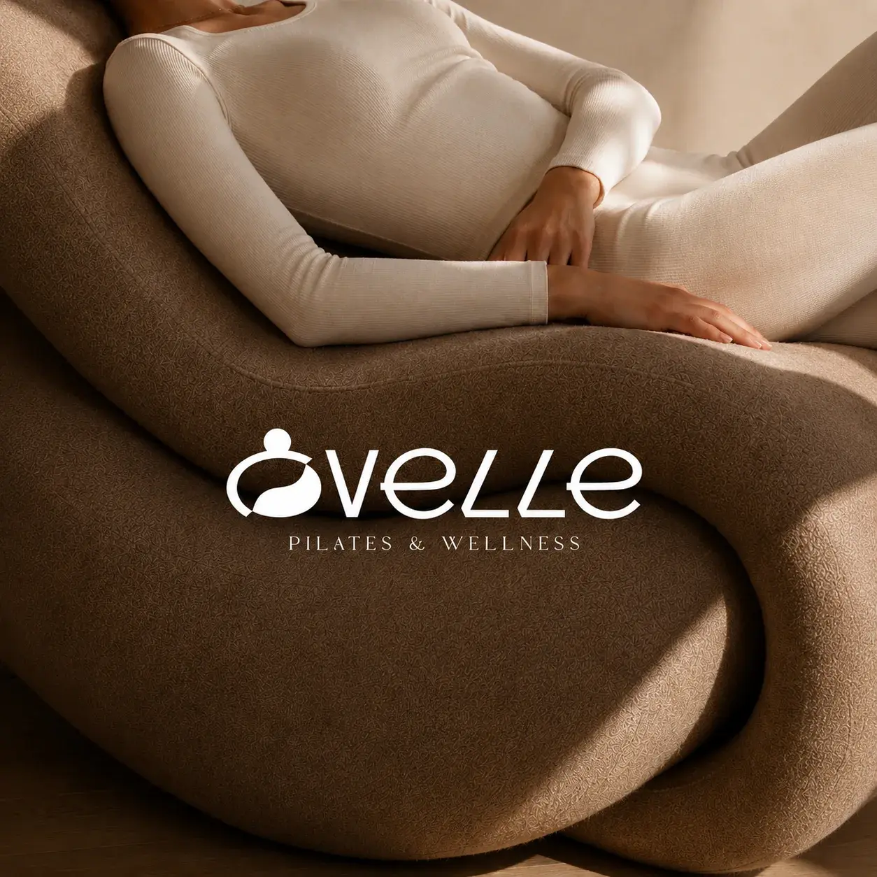 Ovelle Pilates and Wellness wordmark over a warm brown sculptural lounge chair and neutral activewear.