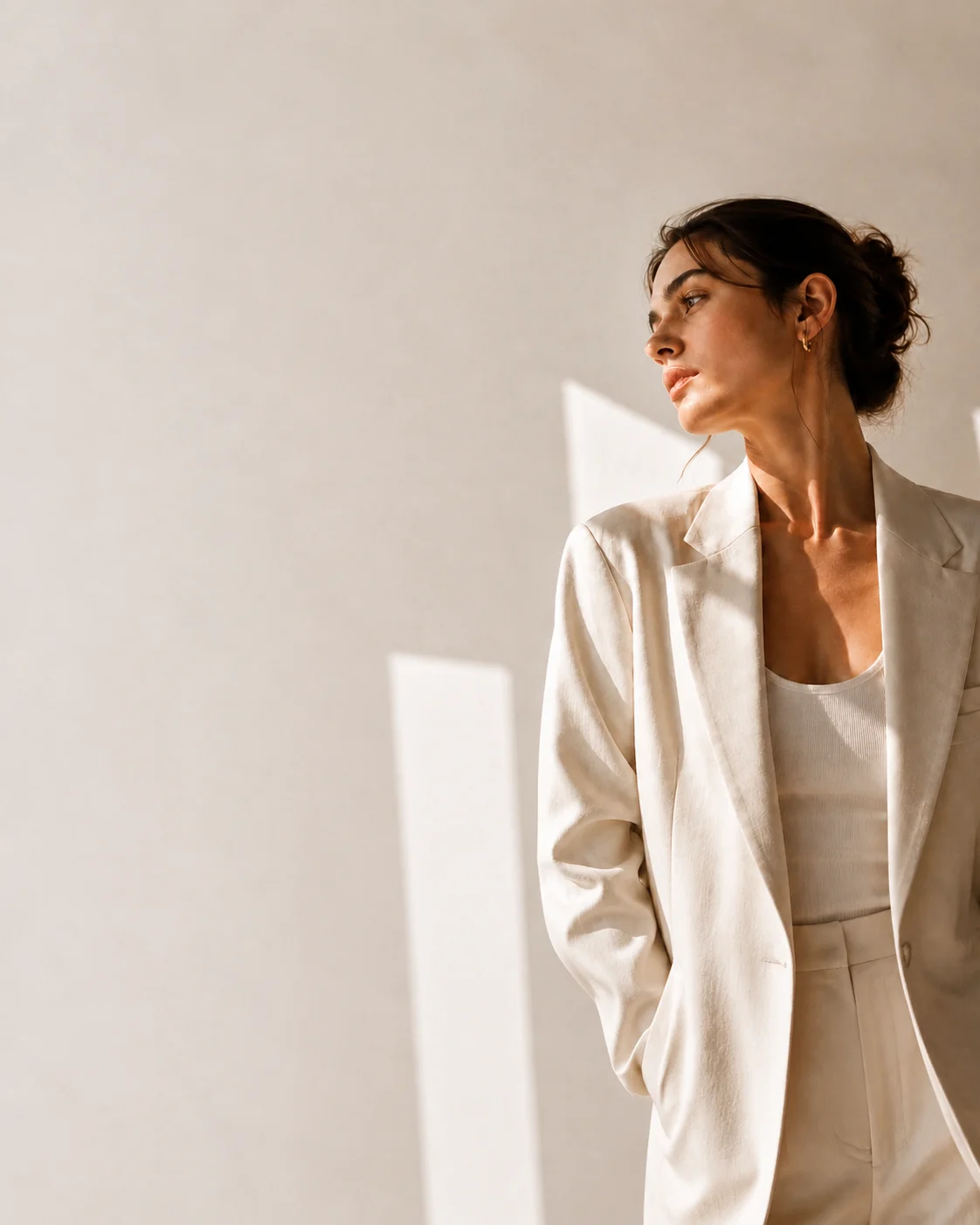 Editorial campaign portrait of a creative professional in an ivory blazer against a sunlit studio wall.